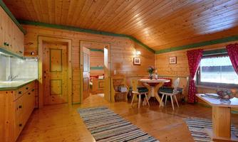 A cozy wooden house with an inviting living area. The space is bright and cheerful with a dining table, a kitchen corner, and a carpet.