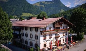 A traditional Tyrolean inn in the mountains with a picturesque view of the surrounding mountains and the Zahmer Kaiser. The entrance is inviting, adorned with flowers.