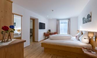 A bright bedroom with wooden details and a large bed. The room is friendly furnished and features a window overlooking the Zahmer Kaiser and the surrounding mountainous landscape.