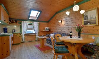 A cozy living area with wooden paneling and a table. The kitchen is well-equipped and there is a pleasant atmosphere with plenty of natural light.