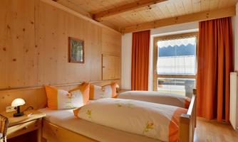 A cozy bedroom with wooden paneling and two beds. Large windows with orange curtains provide plenty of light and a welcoming atmosphere.