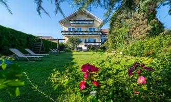 A beautiful house with a large garden and colorful flowers. In the background, there are loungers and a clear sky.