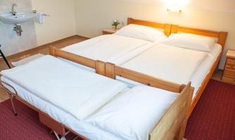 A simple and cozy bedroom with a double bed and a pull-out bed. The walls are painted light and there is subtle lighting.