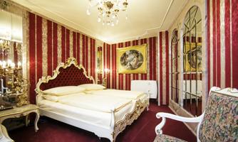 An elegant bedroom with a red striped pattern and opulent furniture. The room is decorated with a chandelier and ornate pictures.