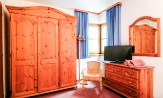 A cozy bedroom with a wooden box and a mirror. A TV stands on a dresser, and there is a chair in the corner.