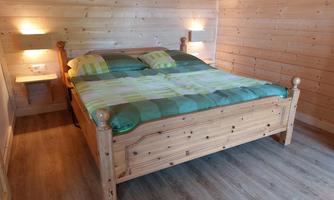 A cozy bedroom with a wooden bed and colorful pillows. The walls are made of light wood and there are night lamps on both sides of the bed.