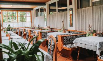 An inviting restaurant with wooden chairs and tables covered with tablecloths. Large windows provide plenty of daylight and a pleasant atmosphere.