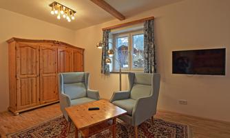 A cozy living room with two blue armchairs and a wooden table. In the background, there is a TV and a wooden cabinet.