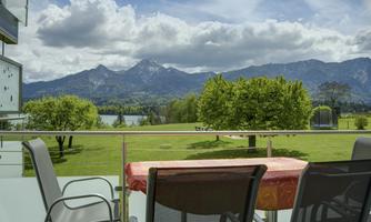 A beautiful view from a balcony overlooking green meadows and impressive mountains. The sky is cloudy and the landscape is very picturesque.