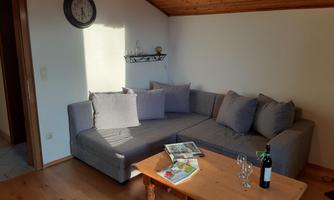A cozy living room with a gray sofa and wooden floor. On the table, there are some magazines and a bottle of wine with glasses.