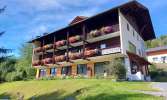 A charming house with a balcony, adorned with colorful flowers. It stands on a hill, surrounded by green nature and blue sky.