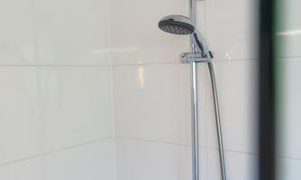 Modern shower with a large rain shower head and hand-held shower in front of light tiles – perfect for relaxing after a day at the beach or a hike.