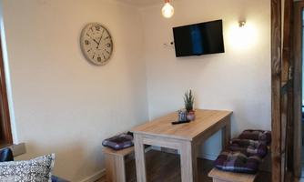 A cozy dining area with a wooden table and benches. A clock hangs on the wall, and a television is also available.