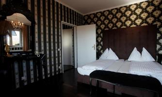An elegant room with classic wallpaper and a double bed. The space is well-lit and features a large mirror.