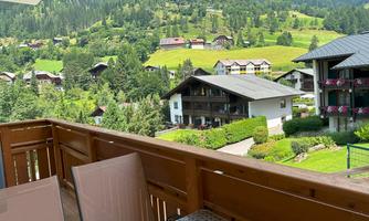 A view from a balcony overlooking a green landscape with hills and houses. The surroundings are calm and idyllic.