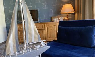 A sailboat model is on a table in a cozy room. In the background, a lamp and a wooden dresser can be seen.