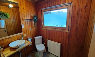 A modern bathroom with wooden paneling and a large window. The furnishings include a sink, a toilet, and a heating system.