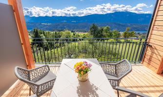 A cozy terrace with a table and two chairs. In the background, a stunning mountain landscape appears under a clear blue sky.