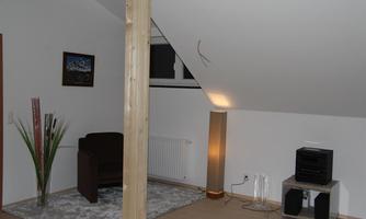 A cozy living space under the roof with a gray carpet and a comfortable armchair. There are decorative plants and a modern floor lamp.