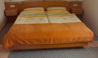 A cozy bedroom with a double bed and orange blankets. The floor is covered with a gray carpet.