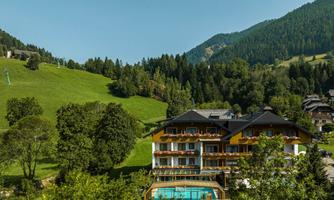 A charming hotel nestled in the green mountains, surrounded by trees and meadows. The outdoor pool invites you to relax.