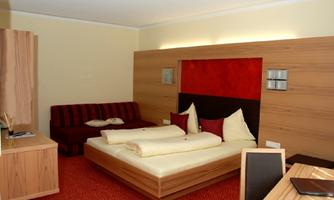 A cozy hotel room with a double bed and a sofa. The walls are designed to look like wood and the decor is simple and modern.