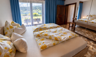 A cozy bedroom with a large bed and colorful pillows. Large windows offer a view of the landscape.