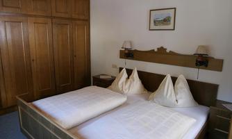 A cozy bedroom with a double bed and two large pillows. The room has a wooden wardrobe and a simple wall picture.