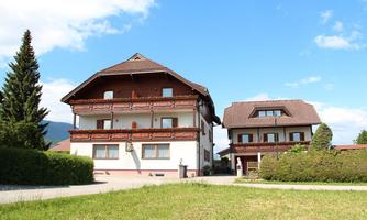 Two traditional houses with wooden decorations in a quiet environment. The sky is blue and there is a lot of greenery in the garden.