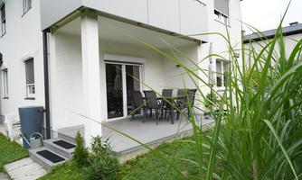 A modern terrace with a dining table and chairs. Surrounded by green landscape and a well-kept garden.