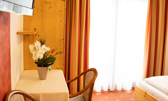 A cozy room with a table and two chairs. A flower vase adorns the tablecloth, while the window lets in daylight.