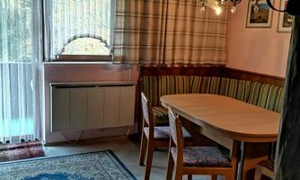 A cozy dining area with a round table and wooden chairs. The room has large windows with curtains and a beautiful carpet.