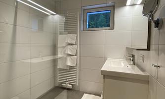 A modern bathroom with a glass shower and a sink. The walls are brightly tiled and there is a window with a view.