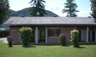 A simple house surrounded by green spaces and trees. Gentle hills can be seen in the background.