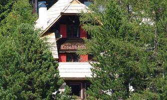 A cozy wooden house with red windows, surrounded by green trees. The natural setting gives the image a tranquil atmosphere.