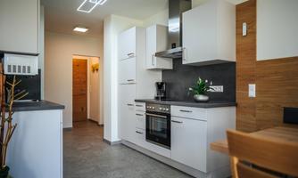 A modern kitchen with white cabinets and a black work area. In the background, there is a door and a plant on the countertop.