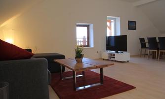 A cozy living room with a gray sofa and a wooden table. A television is placed on a white piece of furniture next to a plant.