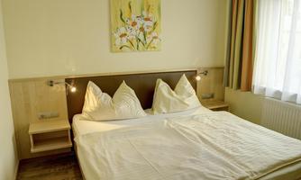 A cozy bedroom with a large double bed and two pillows. White walls and a window create a bright atmosphere.