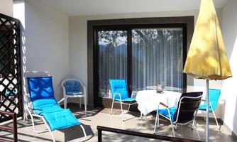A cozy balcony with blue loungers and a white table. A yellow umbrella is ready for shade.