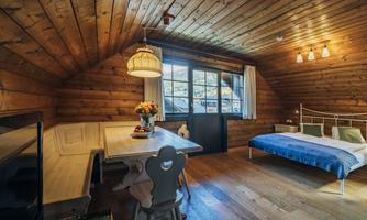 A cozy room with wood paneling, a bed, and a table. The window offers a view of nature, and a flower vase adds an inviting touch.