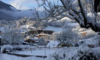 A winter landscape with snow-covered mountains and beautiful chalets. The trees are also covered with snow, and the sky is partly cloudy.