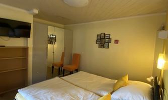 A cozy hotel room with two single beds and colorful pillows. The walls are painted in soft colors and a television is visible.
