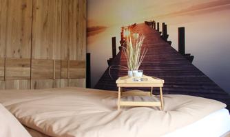 A cozy bedroom with wooden decor. In the background, there is a large wallpaper of a romantic pier at sunset.