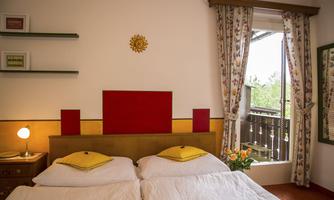 A cozy room with a double bed and colorful cushions. The windows offer a view of nature, and fresh flowers are on the table.