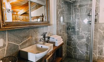 A modern bathroom with a sink and a shower. The walls are covered with gray stones and there is a wooden chest of drawers with fresh towels.