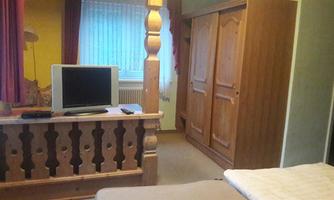 A simple room with a TV and a wooden wardrobe. The walls are in soft colors, and the window has curtains.