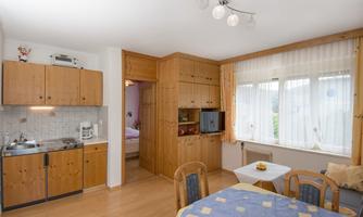 A bright kitchen with wooden cabinets and a dining table. Plenty of light pours into the room through large windows.
