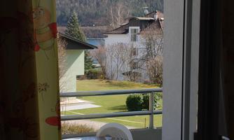 A view from a balcony with a small table and chairs. In the background, green hills and some buildings can be seen.