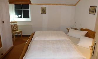 A cozy bedroom with a double bed and a window. There is also a chair and a wooden combination with cabinets.