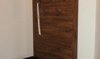 A wooden coat rack with hooks and a bench. The cupboard has a simple and modern design.